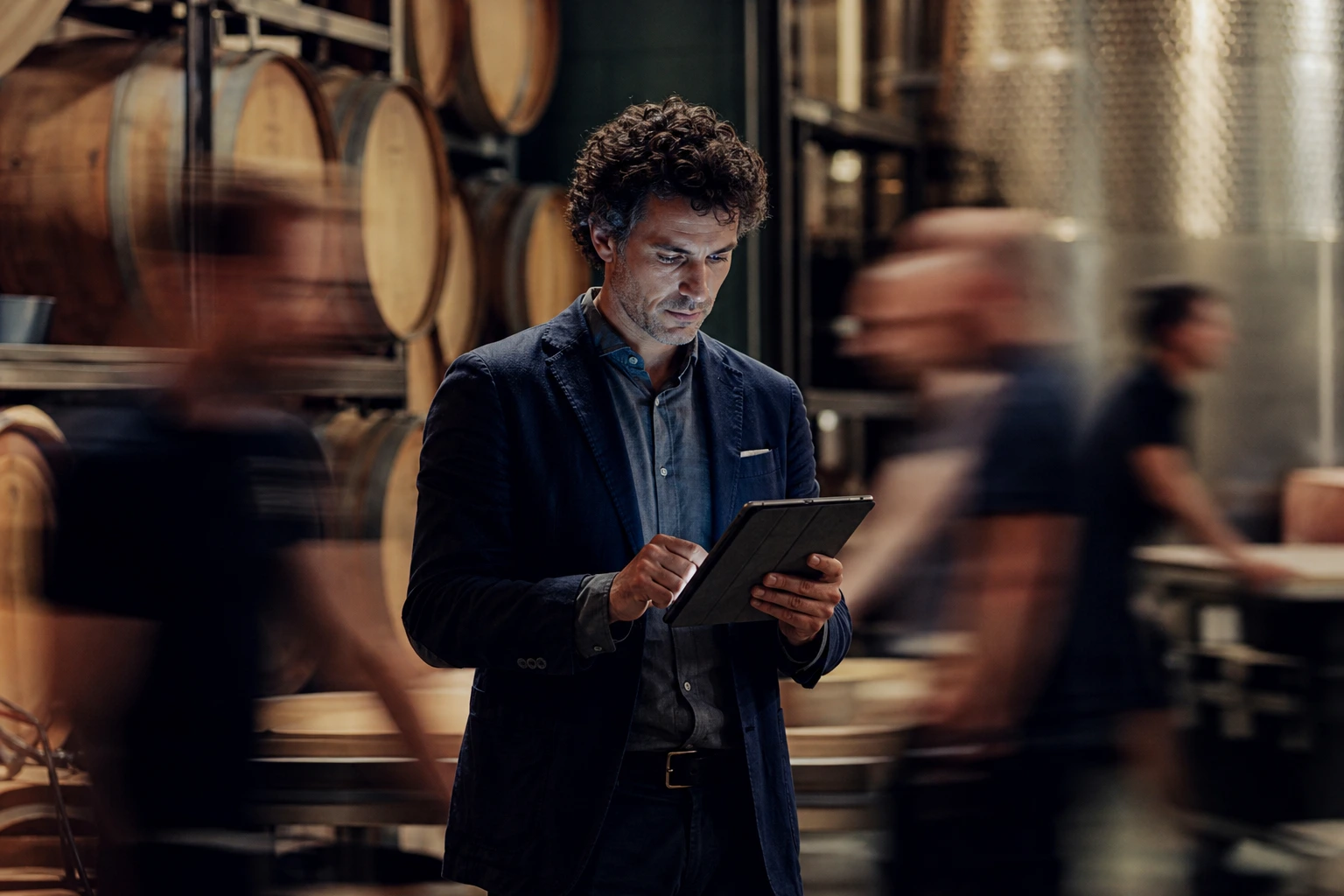 Un uomo si trova in una cantina di vini e consulta i dati sul suo tablet mentre attorno a lui le attività vengono svolte rapidamente grazie alla digitalizzazione.